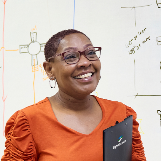 Smiling Upchurch employee holding a clipboard in front of a whiteboard