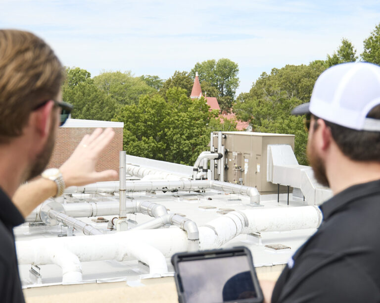 Two workers examining the rooftop systems of a facility